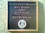 لوحة على قاعدة تمثال ماري بروگر هاي‌ماركت التذكاري. لاحظ أن اسم Mayor رتشارد م. دالي قد تعرض للتخريب وكذلك ختم مدينة شيكاغو[5] كُتب عليه باليد ورسم رمز الأناركية "circle-A".