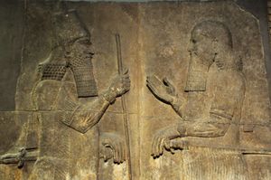 A stone relief showing Sargon II on the left wearing a crown and holding a staff facing a man on the right