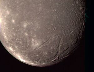 the bottom hemisphere of Ariel is seen, reddish and dark, with cracks and craters lining the edge