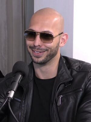 A bald man with a beard and sunglasses smiles at something off-camera.