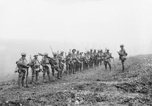 A line of soldiers in battle equipment face another soldier who is addressing them on a gentle slope. Behind them smoke or fog obscures the rest of the terrain.