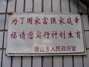 A white sign with two lines of red Chinese characters and a smaller one beneath them on a background of white tile